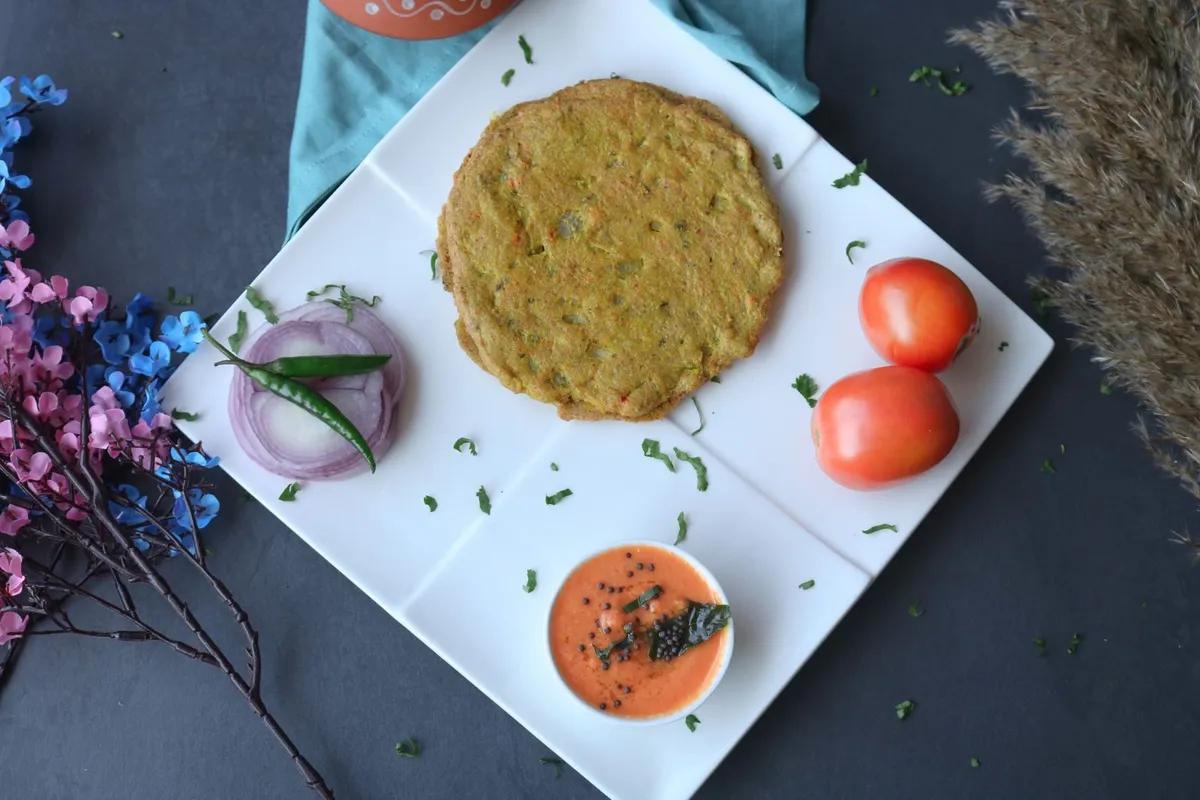 Two moong dal chillas on a plate with a side of curd