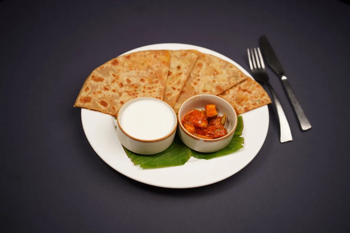 A paneer paratha on a plate with a side of curd