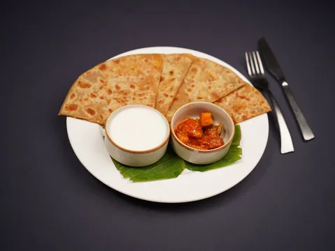 A paneer paratha on a plate with a side of curd